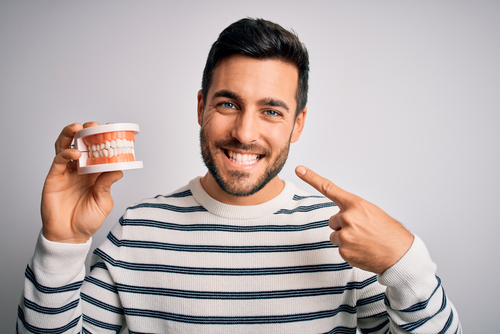 Young,handsome,man,with,beard,holding,plastic,denture,teeth,over