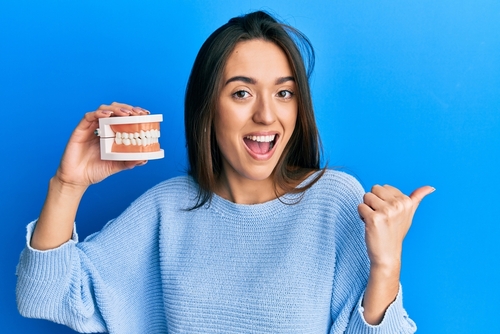 Young,hispanic,girl,holding,denture,pointing,thumb,up,to,the